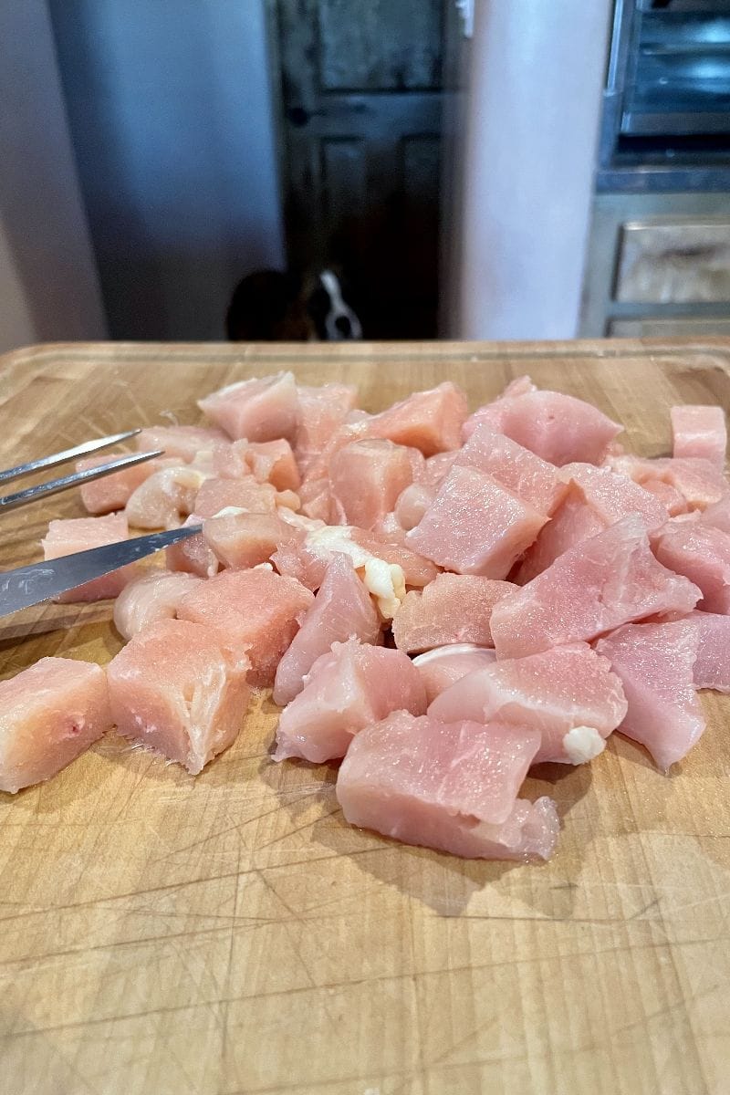 Cubed chicken breast for bourbon chicken on a cutting board.