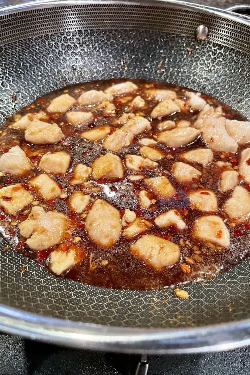 Bourbon chicken cooking in wok in sauce.