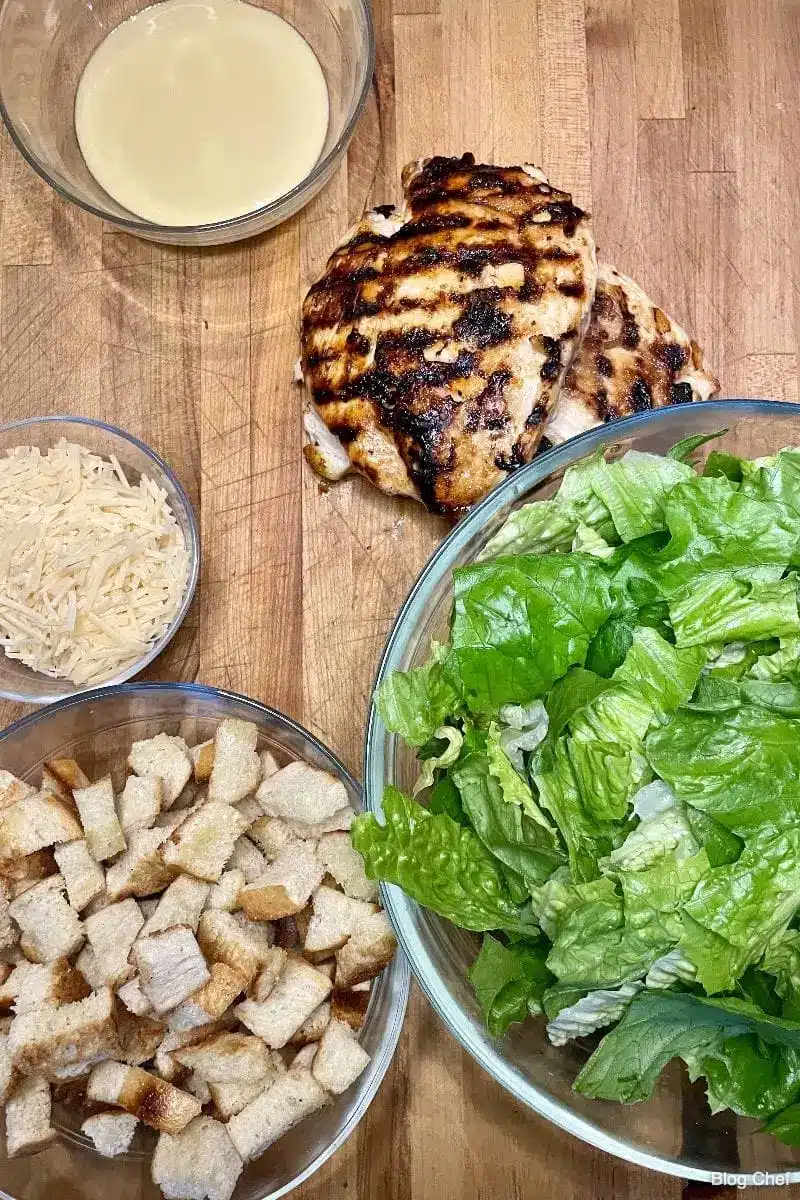 Ingredients for chicken Caesar salad on a cutting board. 