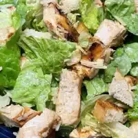 Top view of prepared chicken Caesar salad on blue plate.