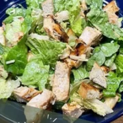 Top view of prepared chicken Caesar salad on blue plate.