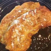 French toast on plate with powdered sugar and syrup.