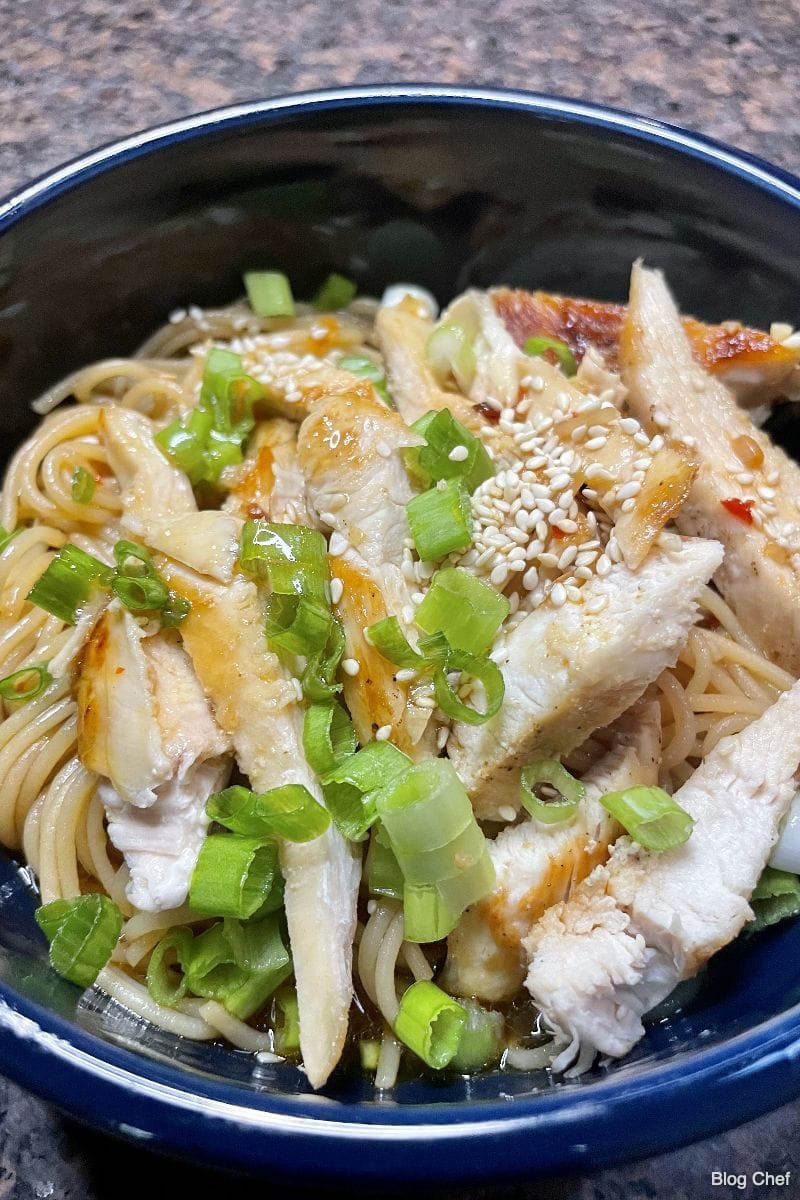 Prepared sesame noodles with chicken on cutting board.