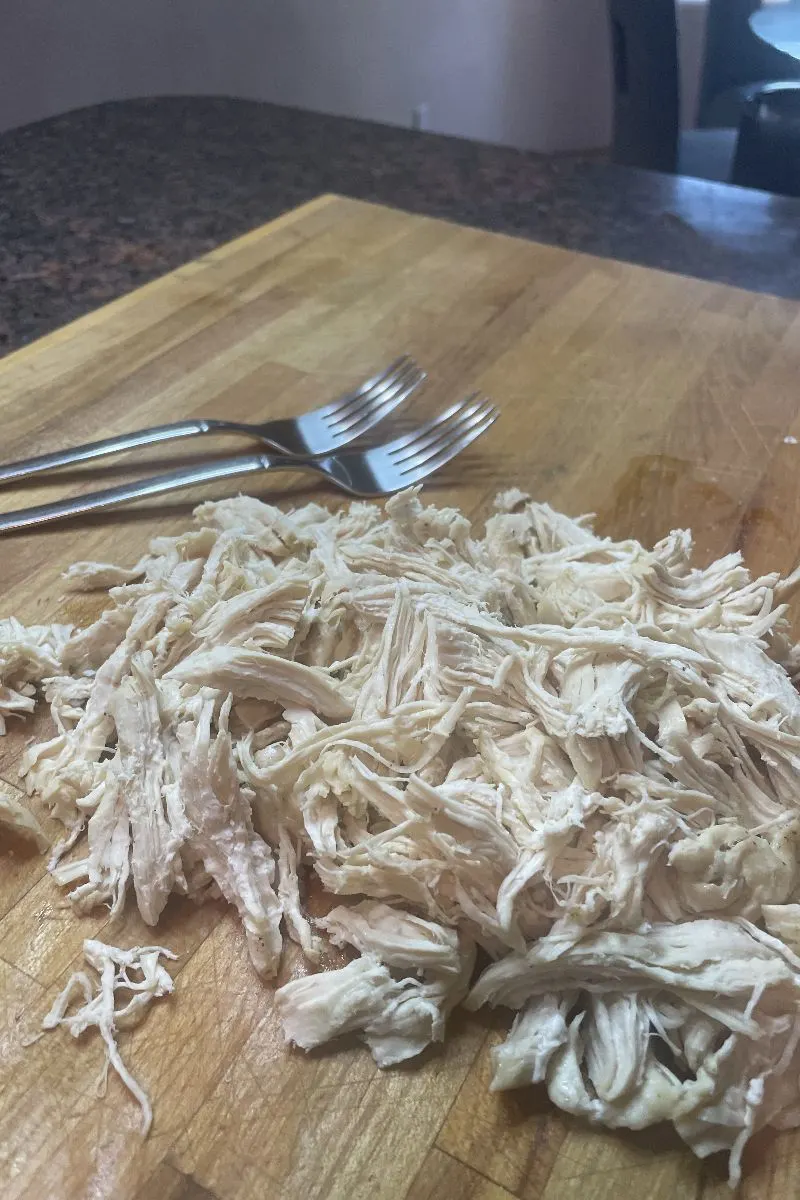 Shredded chicken and two forks on a cutting board.
