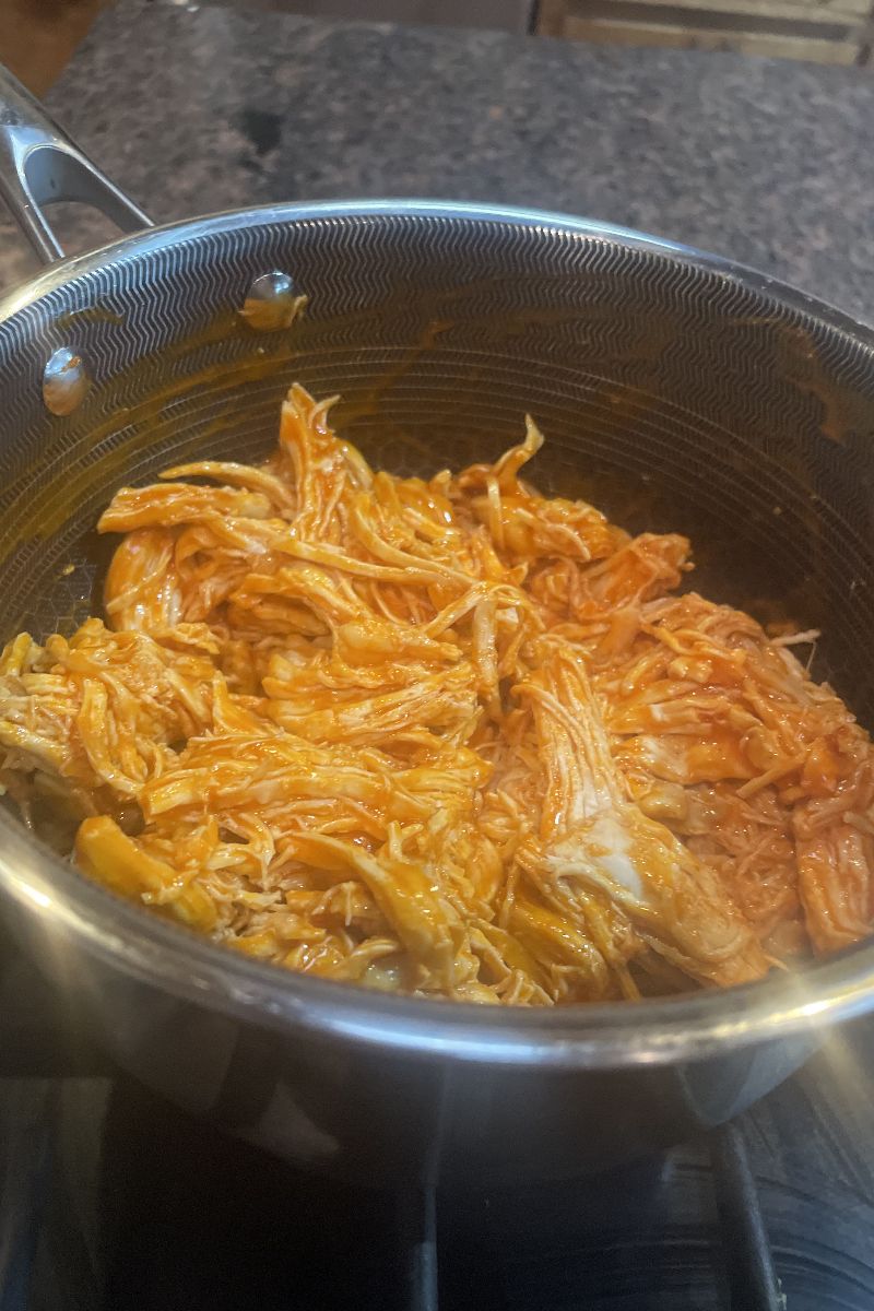 Shredded chicken in buffalo sauce in a saucepan. 