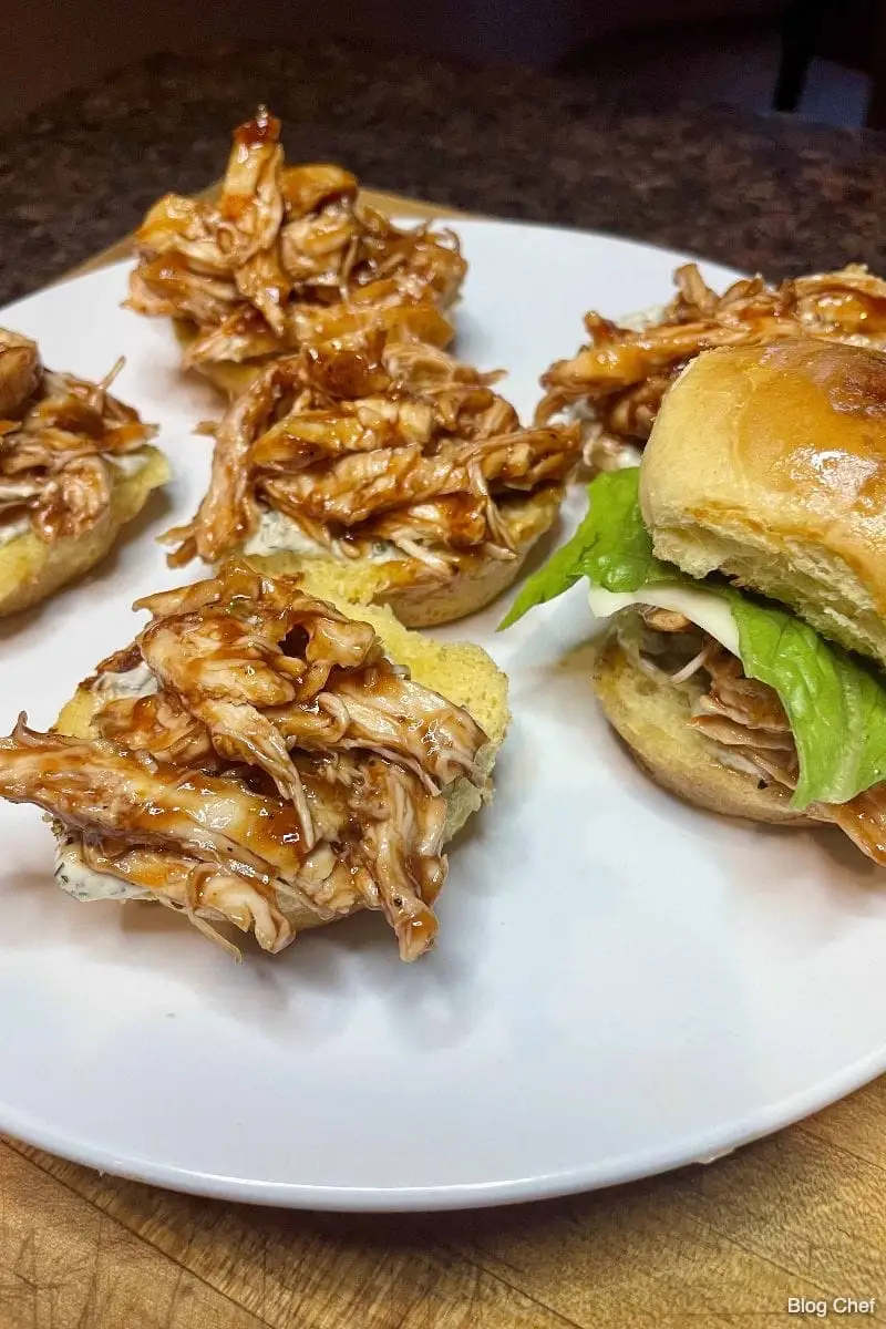 Partially made BBQ chicken sliders on white plate.