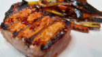 Honey garlic grilled pork chop on white plate with roasted carrots and parsnips.