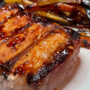 Honey garlic grilled pork chop on white plate with roasted carrots and parsnips.