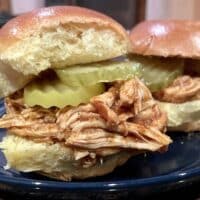Slow cooker pulled chicken prepared in slider buns with pickles.
