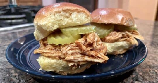 Slow cooker pulled chicken prepared in slider buns with pickles.