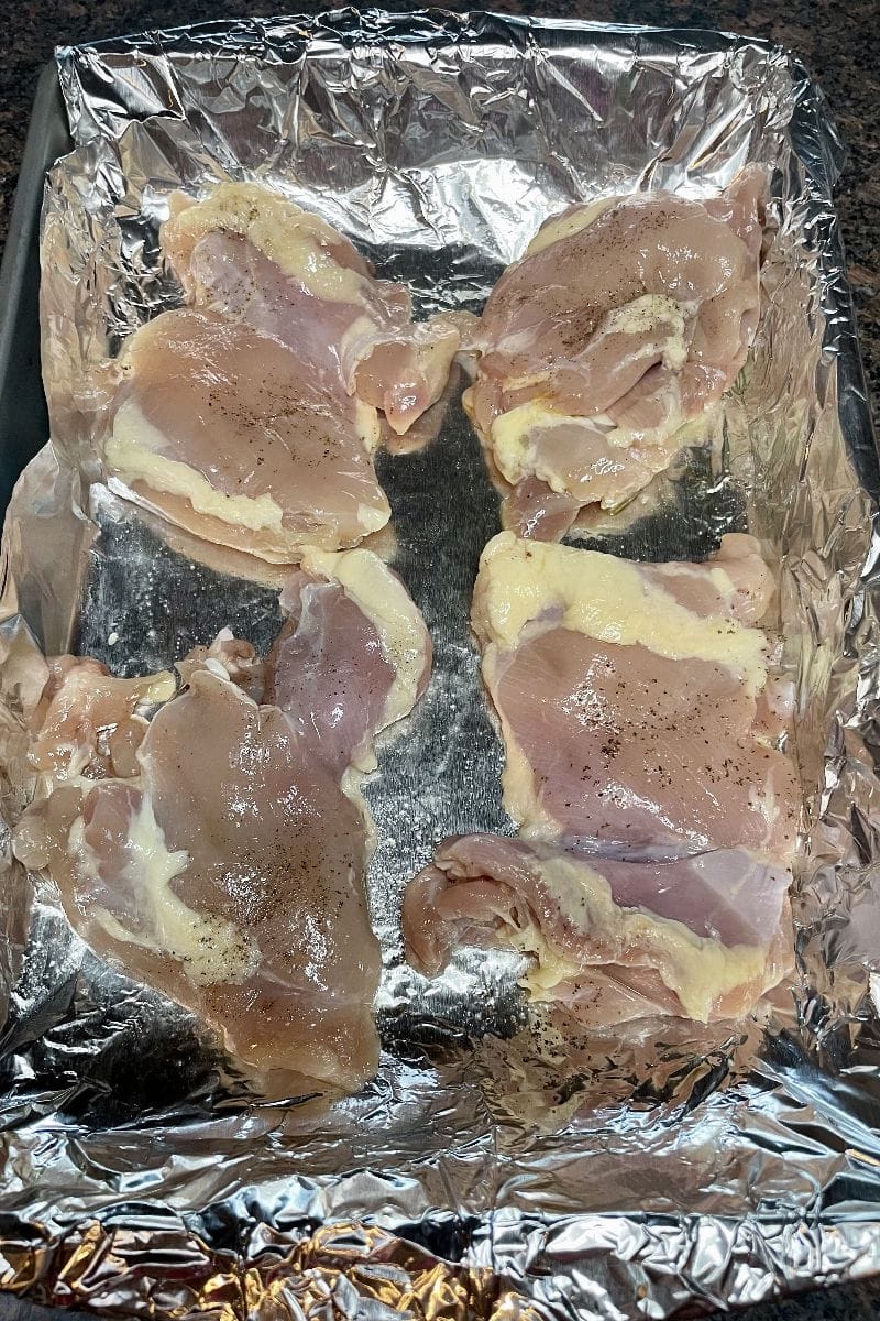 Raw chicken thighs in a baking dish with foil.