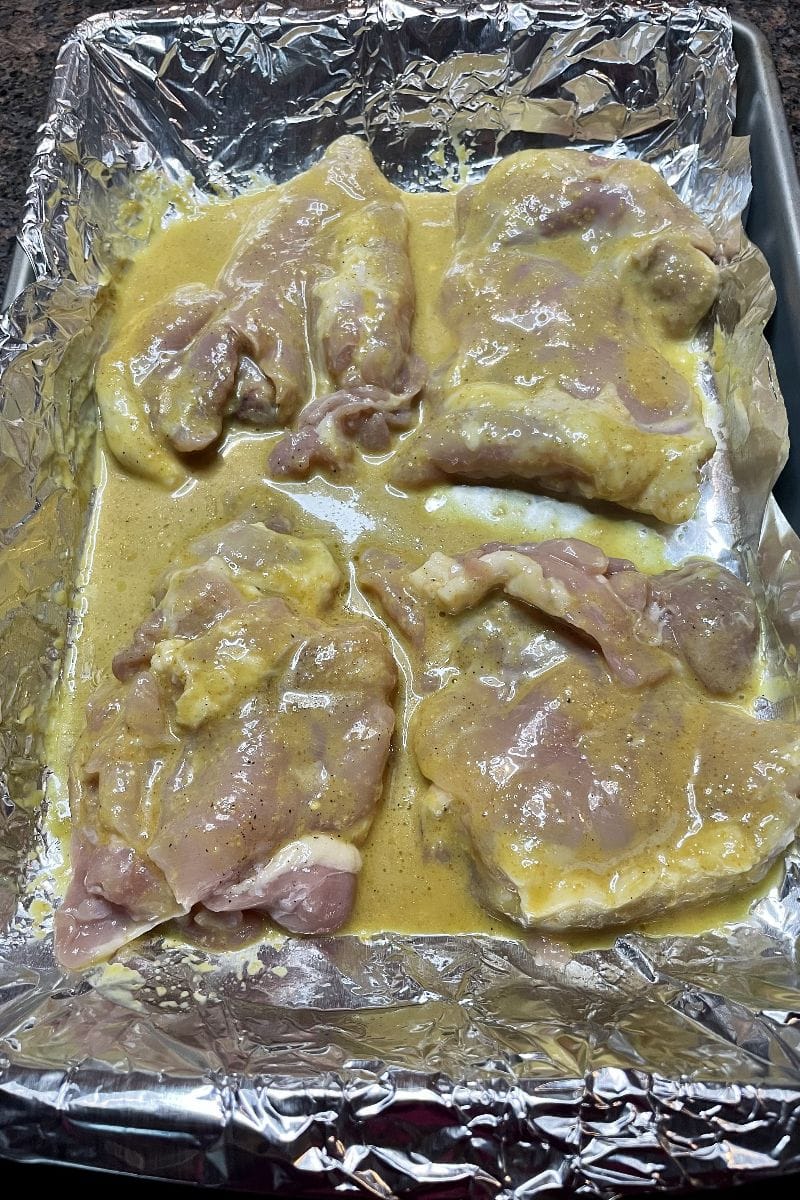 Raw chicken thighs coated in sauce in a baking dish.