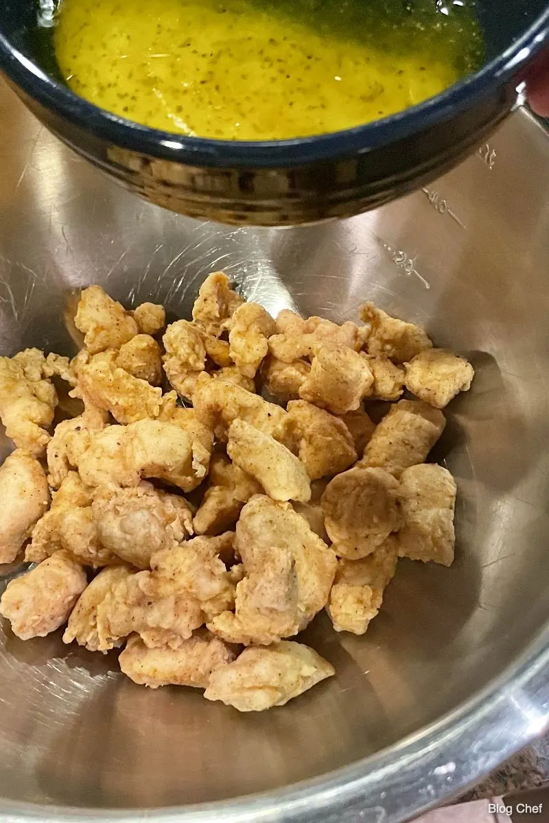 Fried chicken pieces in a bowl with lemon pepper sauce above them. 
