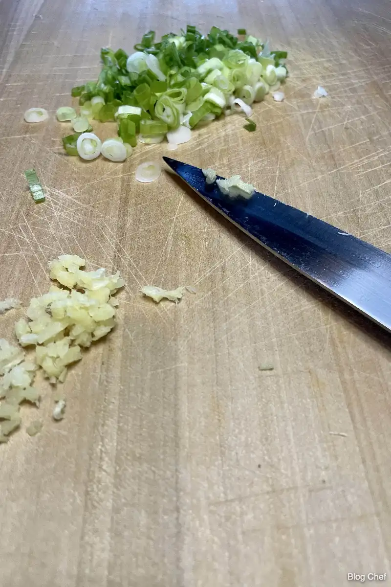 Green onions chopped on cutting board with knife. 