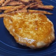 Prepared baked pork chop on plate with sweet potato fries.