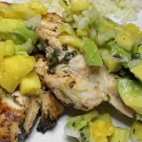 Top view of grilled chicken with avocado salsa on plate with rice.