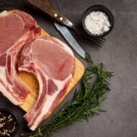 Top view of raw, bone-in pork chops on cutting board.