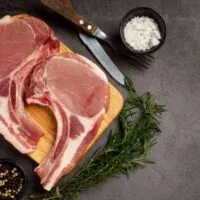 Top view of raw, bone-in pork chops on cutting board.