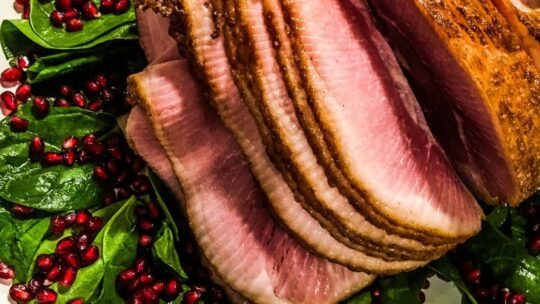Top view of spiral cut ham on top of spinach and pomegranate seeds.