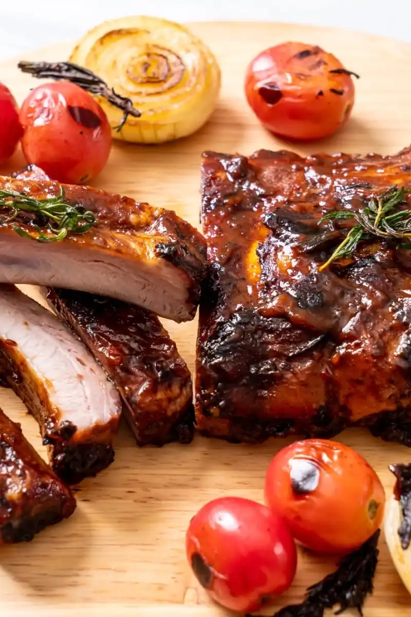 Prepared, oven-baked ribs with tomatoes on serving board.