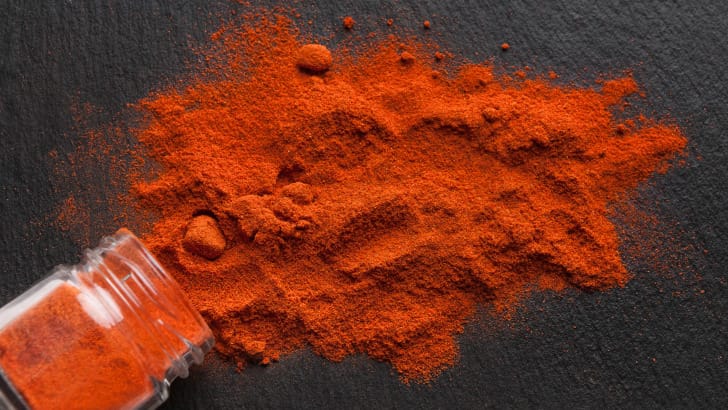 Sweet paprika poured out on black surface.
