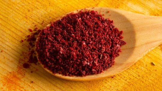 Ground sumac in a spoon on wooden table.