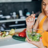 Woman eats salad while smiling.