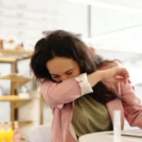 Woman sitting at desk coughs into elbow.