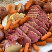 Sliced corned beef on a platter with carrots, onions, and potatoes.