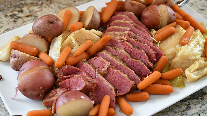 Sliced corned beef on a platter with carrots, onions, and potatoes.