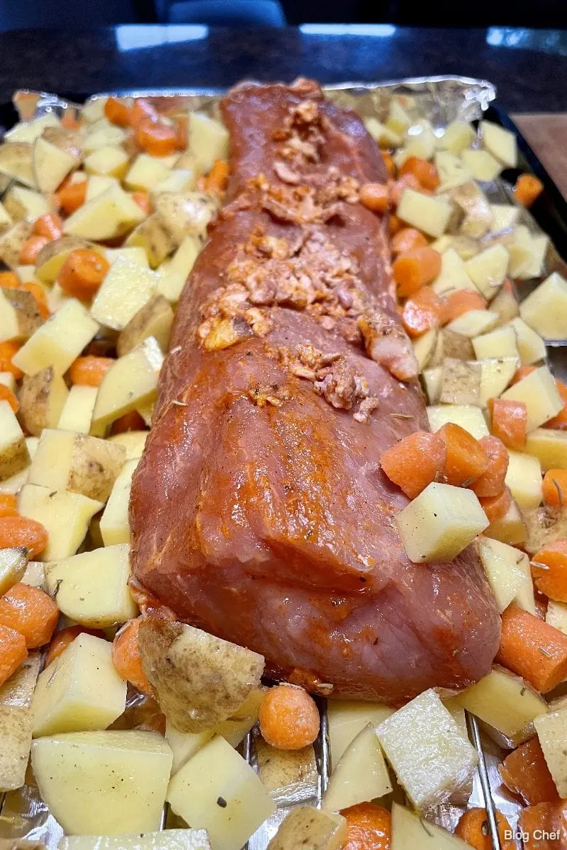 Raw Smithfield pork tenderloin on roasting rack with vegetables. 