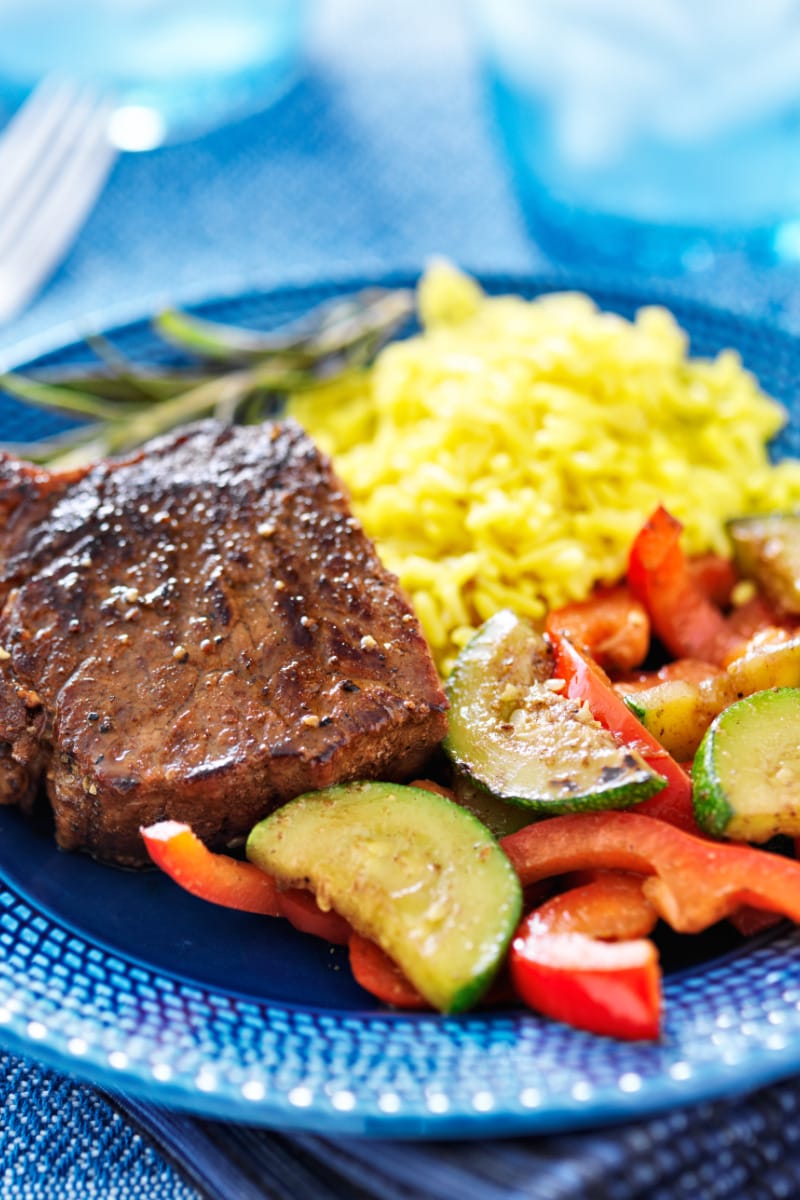Marinated, oven-baked steak on plate with vegetables and rice.