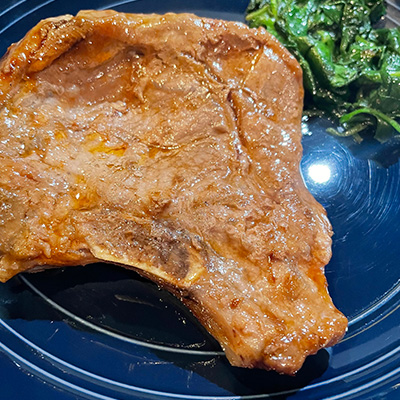 Baked thin pork chop on plate with spinach.