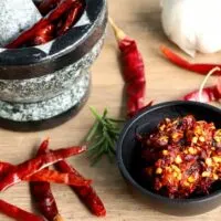 Red chilis and mortar and pestle on wooden surface.