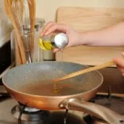 Close up of hand pouring oil into stovetop pan.