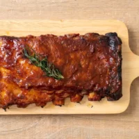 Cooked pork ribs on wooden serving plate.