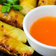Fried eggrolls on serving dish with duck sauce as dipping condiment.