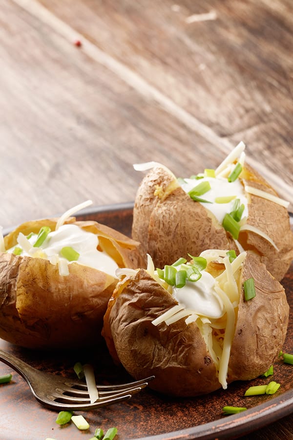 Three baked potatoes with toppings on a plate.