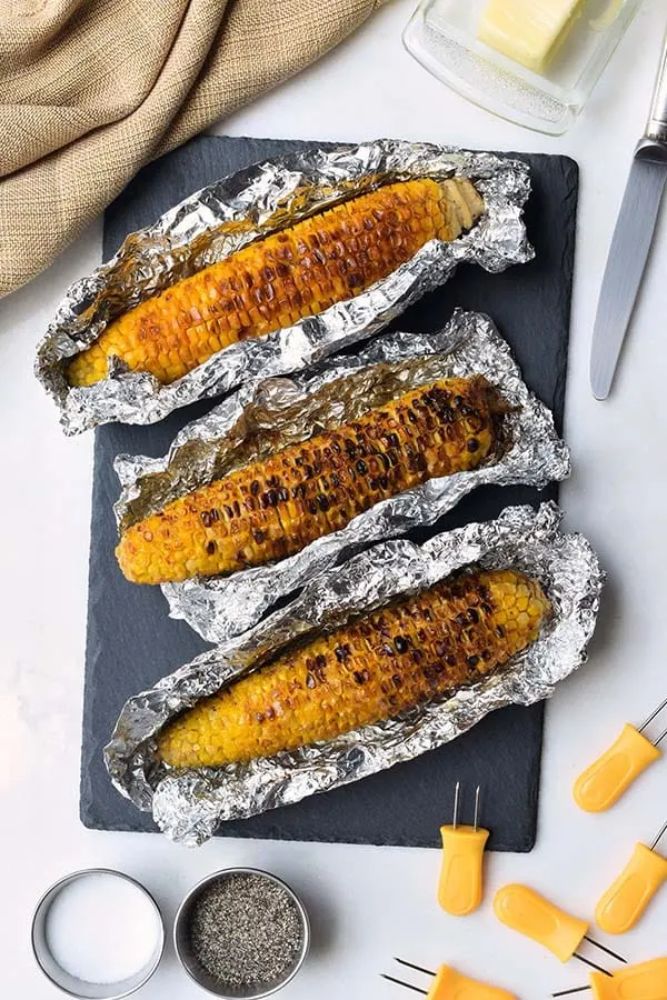 Three ears of grilled corn partially wrapped in foil.