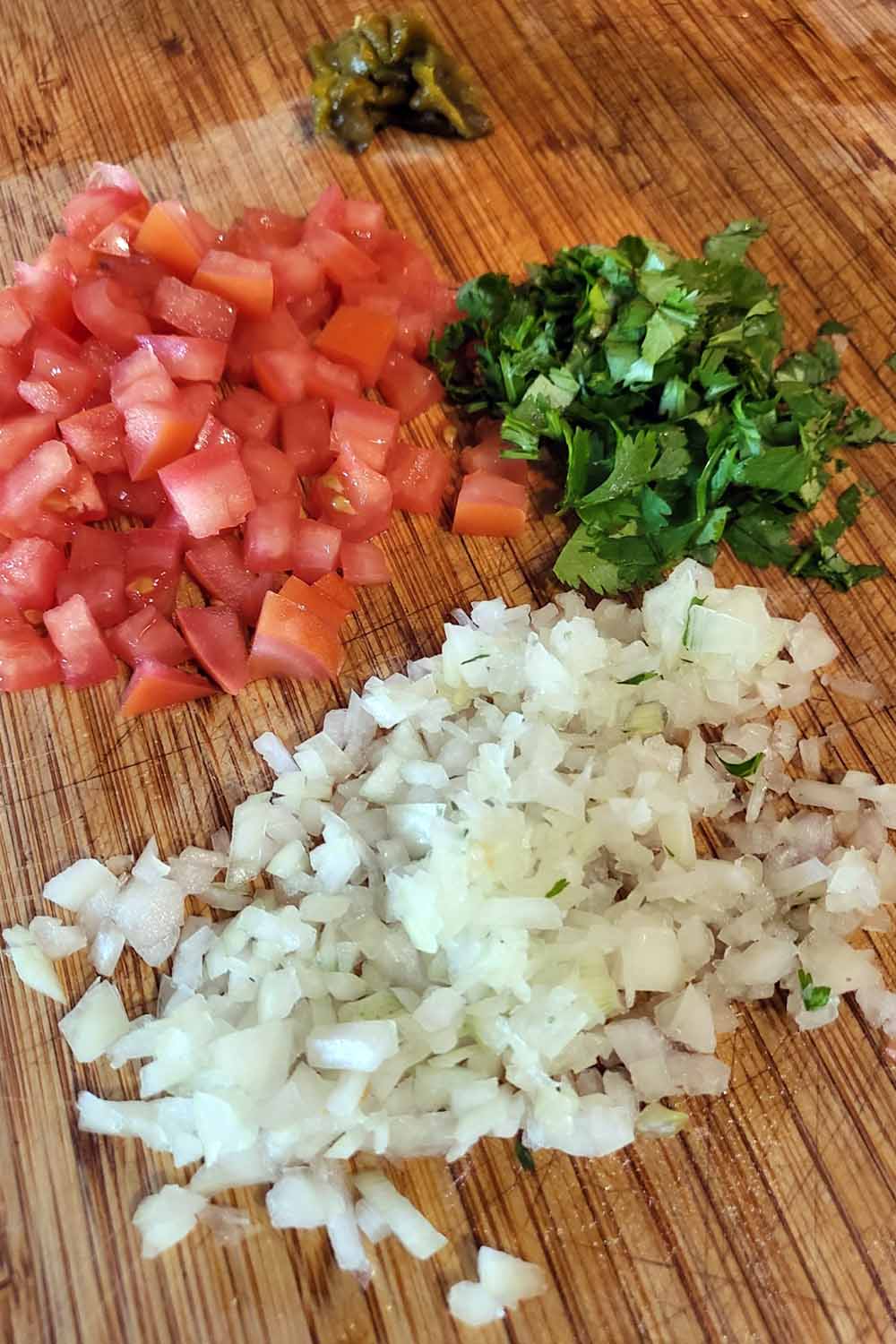 Cutting board with chopped onion, tomato, cilantro, and green chiles.