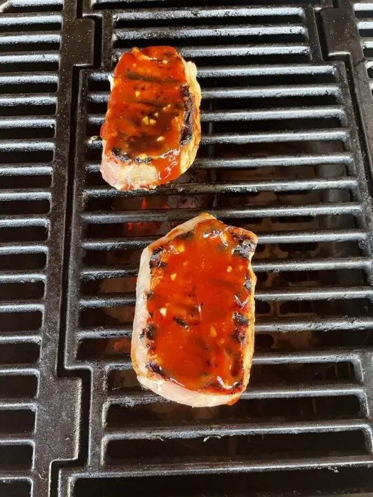 Two pork chops with honey garlic glaze on a grill.