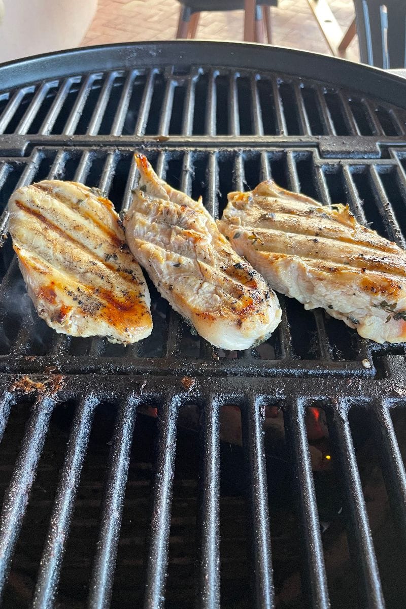 Top view of three chicken breasts on a charcoal grill.