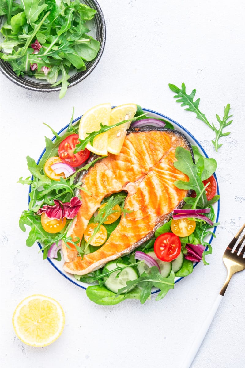 Top view of grilled salmon on plate with arugula salad, a good meal to include in bodybuilding diets.