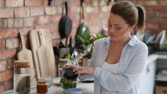 Woman surrounded by eco-friendly kitchen products makes tea.