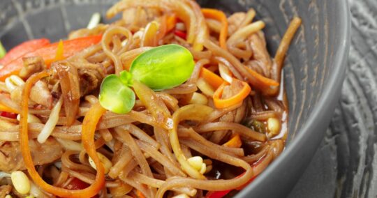 Close-up view of Asian noodles with shredded carrots and meat.