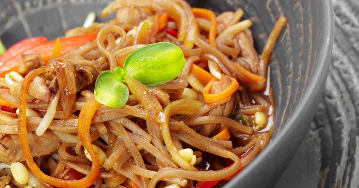 Close-up view of Asian noodles with shredded carrots and meat.