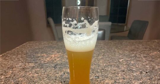 Glass of beer with foamy head on countertop.